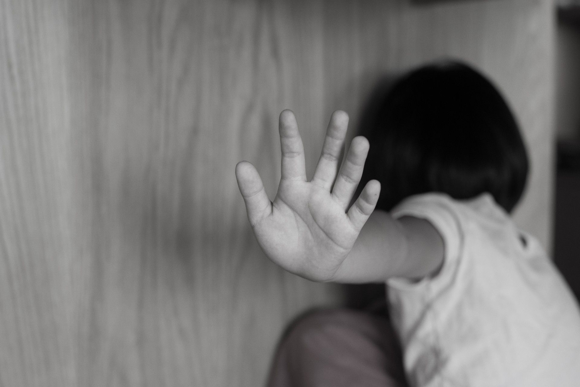Desaturated photo of a child holding their hand up and turning away from the camera - Boys & Girls Club sexual abuse