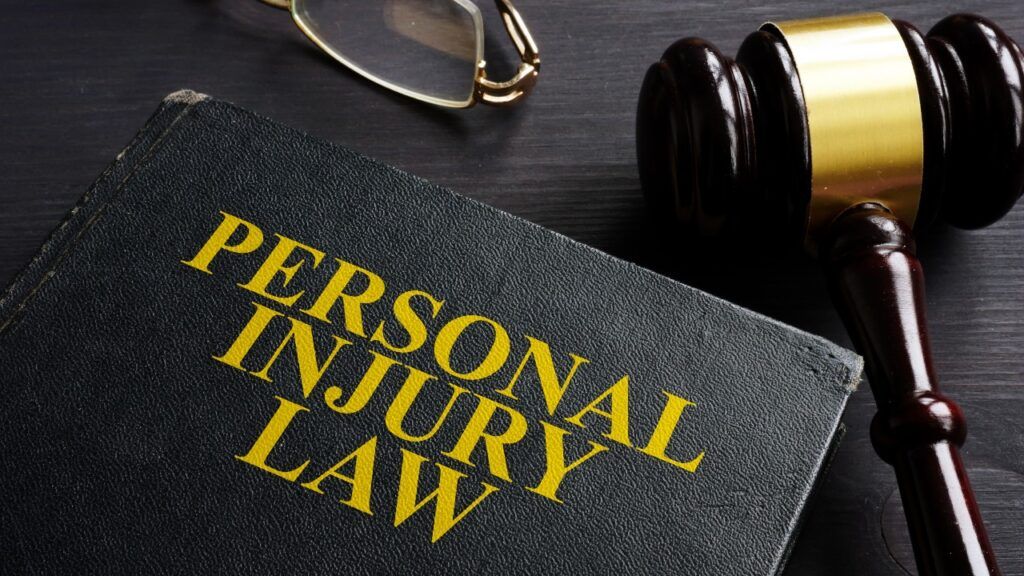 Personal Injury Law book, glasses,  and a gavel on a black desk.