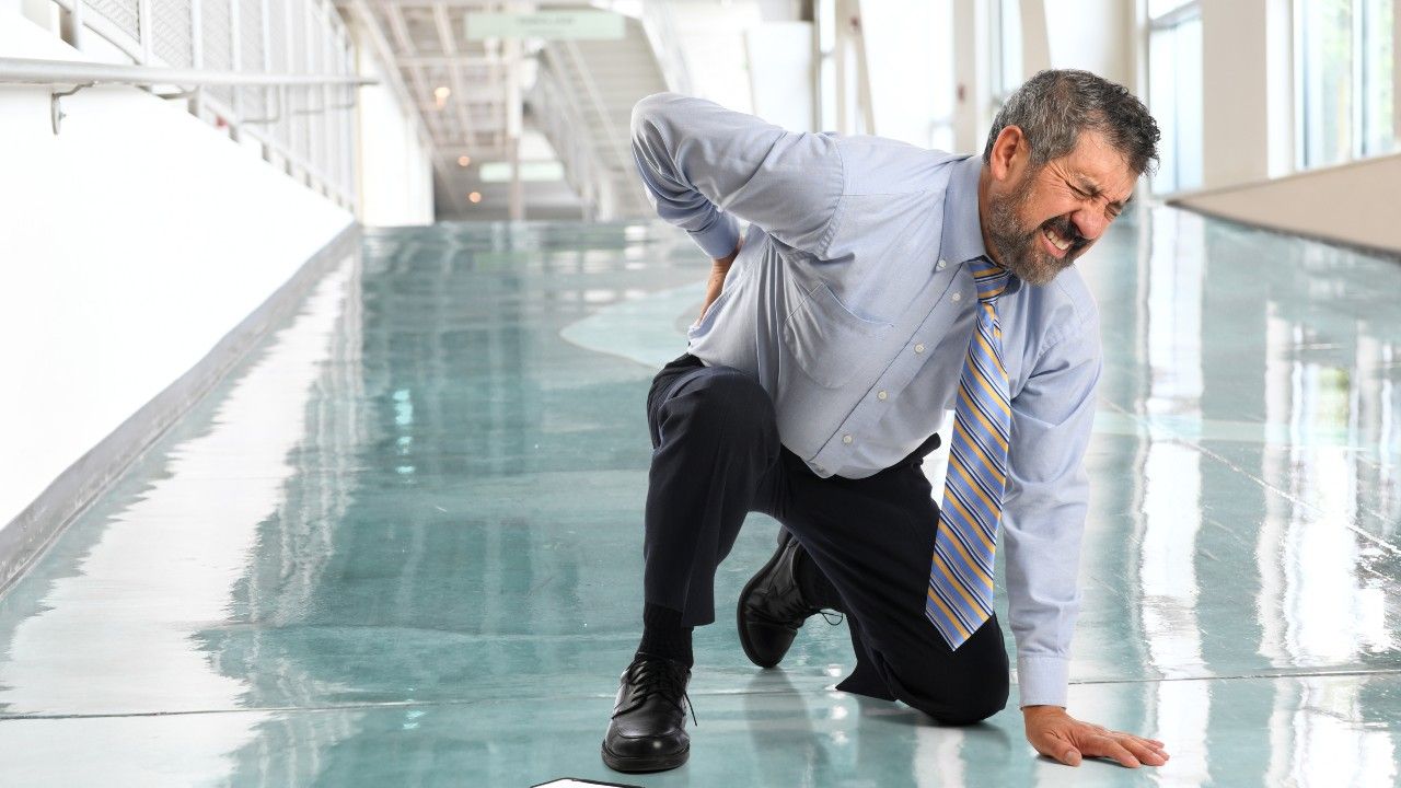 Senior businessman suffering from back injury inside office lobby.